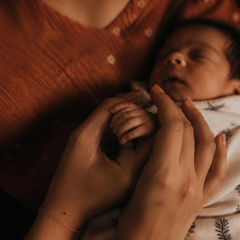 A mother's hands cradling her newborn's hand