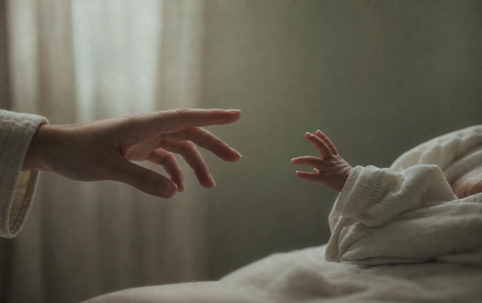 A mother's hand reaching toward her baby's hand as it pulls away